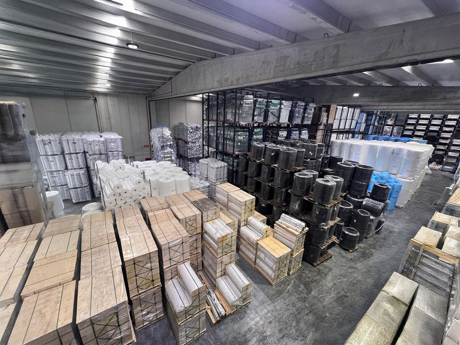 Industrial warehouse interior featuring organized rows of wooden crates and plastic-wrapped rolls on pallets.